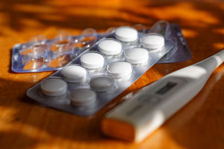 Digital thermometer and tablets in a blister pack on a wooden tableの写真素材