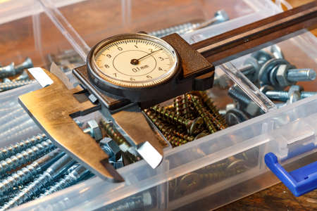 Slide caliper with round scale and screws in storage box on a wooden tableの写真素材