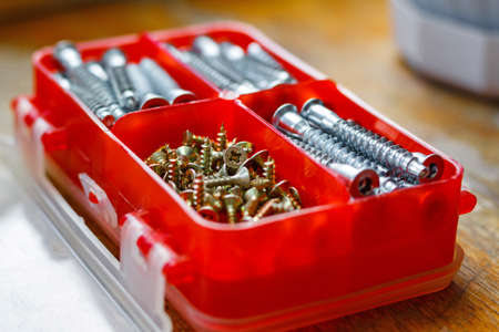Set of fasteners for assembling furniture in a red plastic storage box on a wooden table