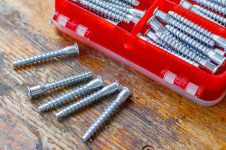 Set of fasteners for assembling furniture in a red plastic storage box on a wooden tableの写真素材