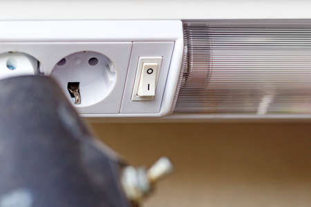 Fragment of fluorescent lamp with built-in socket and switch above workbench in the workshop
