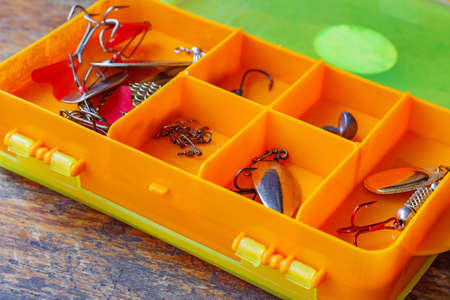 Metal fishing baits in a orange plastic storage box closeupの写真素材