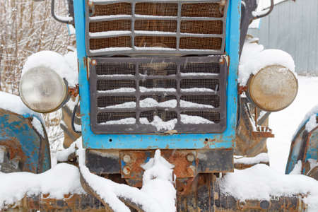 Fragment of the front of an old tractor covered with snow closeup
