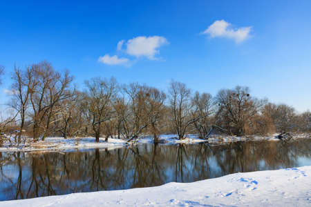 Snow-covered shore of small river against the blue skyの写真素材