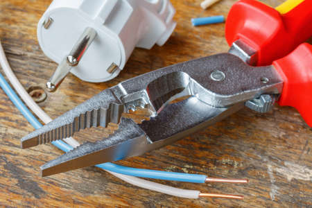 Combination pliers for wiring with electrical plug and copper wires on wooden table in workshop