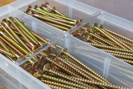 Yellow long screws in opened storage box cells on wooden table in workshopの写真素材