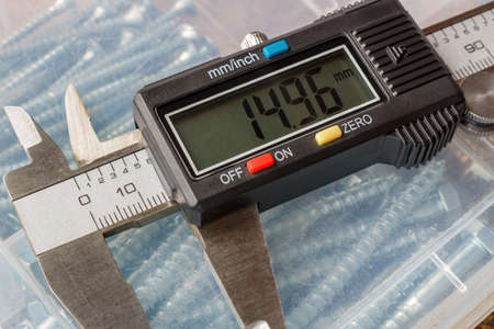 Digital electronic caliper on a background of storage box with hexagon head bolts closeupの写真素材