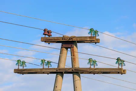 Old concrete power line support with insulators and wires against blue skyの写真素材