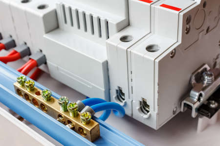 Neutral bus connected by blue wires closeup against automatic circuit breakers in the white plastic mounting boxの写真素材