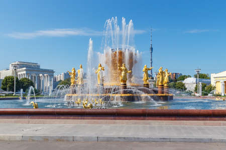 Moscow, Russia - July 22, 2019: Fountain Friendship of Peoples on a background of Ostankinskaya TV tower and pavilions in VDNH park in Moscow at sunny summer day against blue skyのeditorial素材