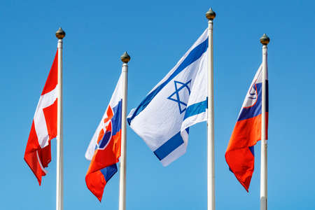 Flags of different countries waves on the wind on flagpole against blue sky in sunlight