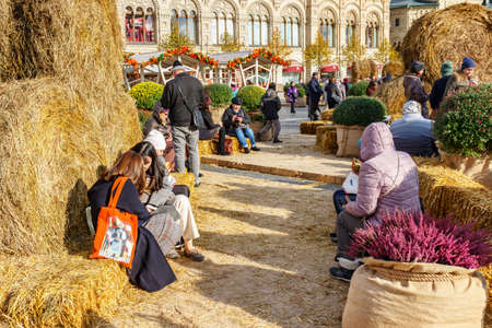 Moscow, Russia - October 08, 2019: People resting on the benches made of straw at sunny autumn day on the traditional festival Golden Autumn on Red Square in Moscow historical centerのeditorial素材