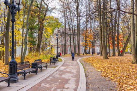 Moscow, Russia - October 16, 2019: Autumn in Tsaritsyno Park in Moscow. Footpath with benches against trees with yellow leaves in sunny autumn dayのeditorial素材