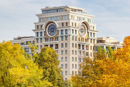Moscow, Russia - October 03, 2019: View of corner tower of modern residential building with big round windows under roof against trees with colored leaves in sunny autumn dayのeditorial素材