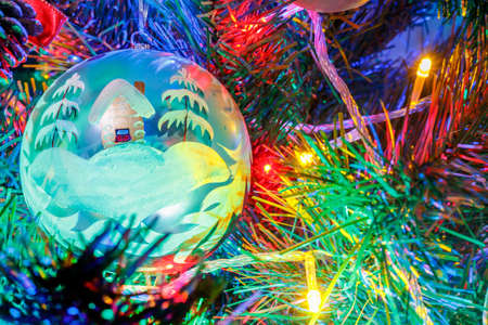 Big christmas ball on the branches of decorative fir in the light of colorful lights of electric...