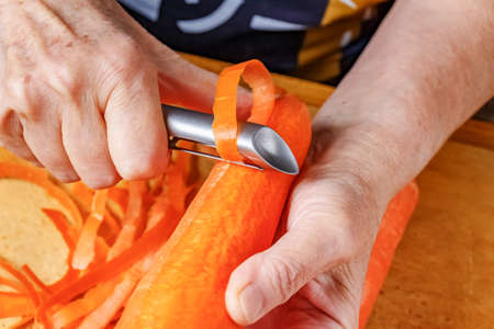 Female hands peeling carrot by peeler for vegetables and fruitsの写真素材
