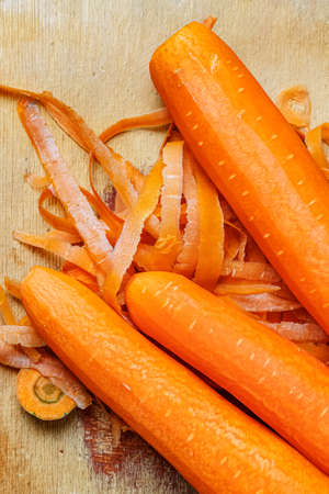 Group of bright orange fresh juicy carrots after removing skin on the wooden cutting board