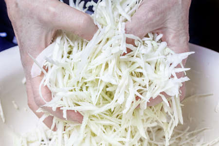 Woman hands mixing shredded cabbage with salt in the metal bowl