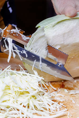 Harvesting cabbage. Woman hand shredding head of fresh juicy white cabbage by knife on the wooden cutting boardの写真素材