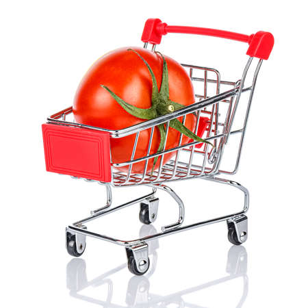 Red ripe tomato with green leaves in the chromed toy market shopping cart with red handle and plastic board on the front. White background with reflection on the glossy glass surfaceの写真素材