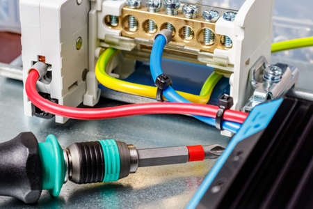 Screwdriver with colored handle lying on metal mounting plate of electrical panel among installed...