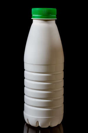 White plastic milk bottle with green cap isolated on black background with reflection on glossy surfaceの写真素材