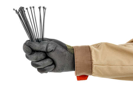 Electrician hand in black protective glove and brown uniform holding black plastic cable ties...