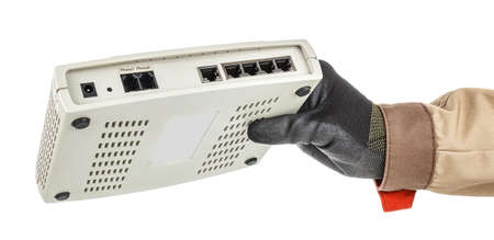 Male hand in black protective glove holding VoIP gateway with connection ports on back panel...