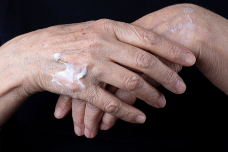 Elderly woman rubs nourishing cream in wrinkled hands close-up on black backgroundの写真素材