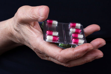 Sealed blister packs with colored pills in palm of elderly woman close-up on black backgroundの写真素材