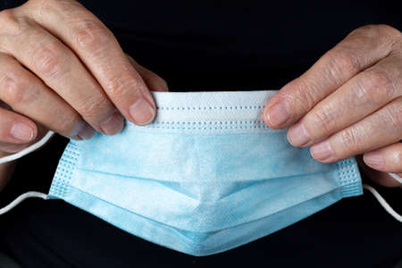 Disposable medical mask in elderly woman hands close-up on black backgroundの写真素材