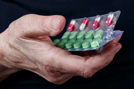 Blister packs with colored pills in elderly woman palm on black backgroundの写真素材
