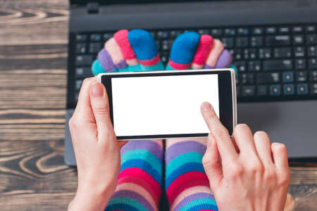 Female hands holding a cell phone, smartphone, with tuchscreen on wooden backgroundの写真素材