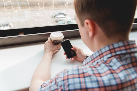 Young man taking a coffee break at cafe touching his smartphone