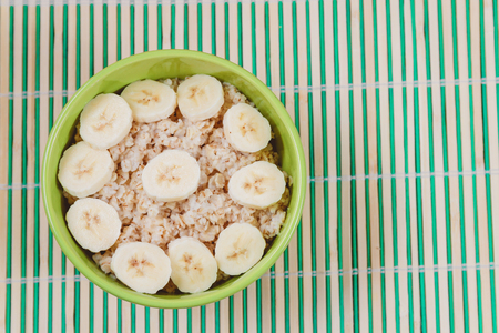 Tasty Oatmeal Porridge with Bananas in Green Bowl. Top view. Heealthy Food Conceptの写真素材