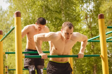young man doing pull ups on horizontal bar outdoors