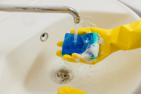 Cleaning Bathroom Faucet with Detergent in Yellow Rubber Gloves with Blue Sponge - Housework, Spring Cleaning Concept.の写真素材