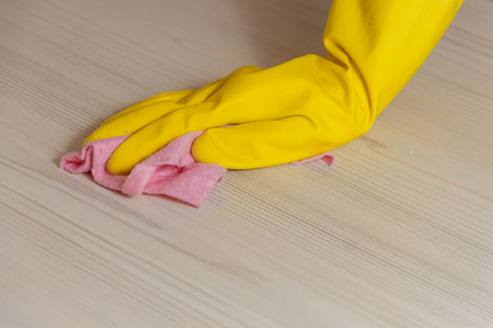 Female Hand in Yellow Glove Cleaning Light Wooden Modern Table with Pink Cloth for Home Maintenance...