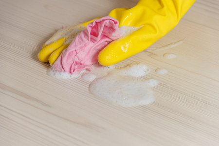 Female Hand in Yellow Glove Cleaning Light Wooden Modern Table with Pink Cloth for Home Maintenance and Housekeeping.の写真素材