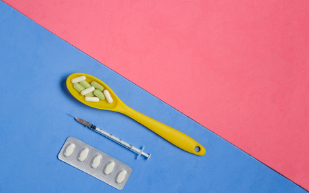 Pills and Capsules in Yellow Spoon, Syringe on Blue Background with Pink Copyspace.の写真素材