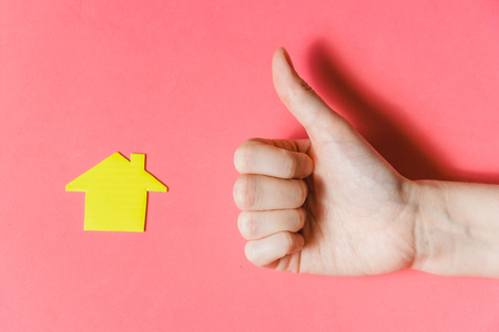 Real Estate Concept. Hand Showing Thumbs up at Miniature House on Pink Backgroundの写真素材