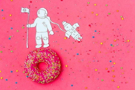 Creative Food Minimalism, Donut in Shape of Planet in Pink Sky with Astronaut, Space Ship Top View,...