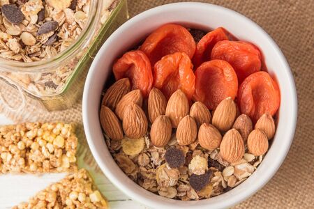 Granola cereal flakes with dried fruit, nuts in green bowl on white wooden table. Top view.の写真素材