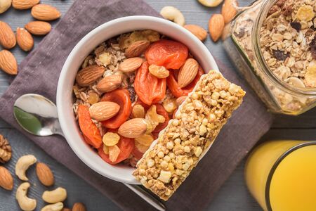 Granola cereal flakes with dried fruit, nuts in green bowl on gray wooden table. Top view.