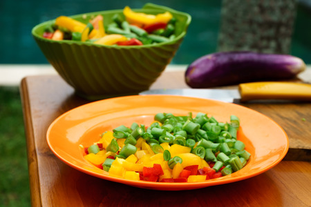culinary workshop. Vegetable salad with own hands in the courtyard of a private house. Preparation of vegetable salad on the background of home garden and pool, cut vegetables, peppers, beans, onions, on a wooden board with female hands of fair skin. Red,の写真素材