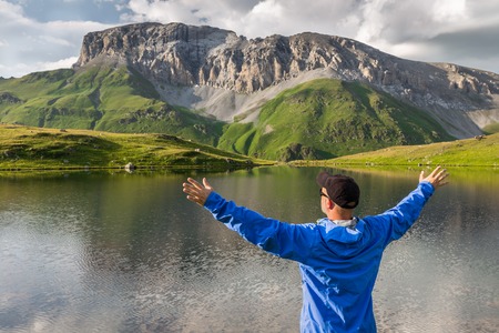 Hiker standing with raised hands near the beautiful mountain lake and enjoying view. Concept of extreme sport and active lifeの写真素材