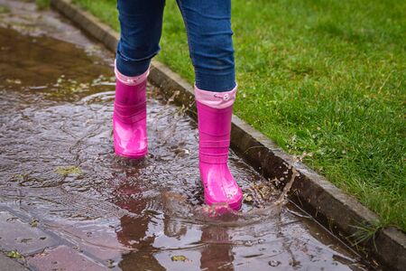 Girl wearing rubber boots standing in a dirty puddle on a summer day. Happy childhood. Having fun outdoorsの写真素材