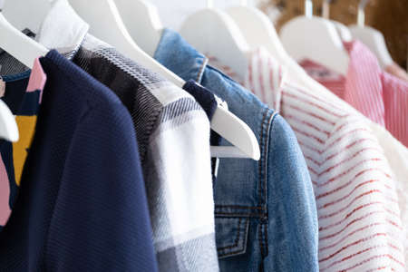 Wooden white hangers with clothes on the rail in the store with womens clothing for sale. Shirt, dress, jacket, vest, jeans. Flea market, second hand, discount, exchange, donationの写真素材