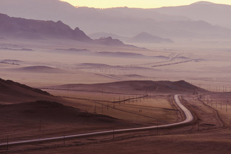 Majestic autumn mountain landscape. Winding road passes by fields and hills, a beautiful foggy...