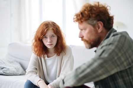 Close up man in front and sad girl with freckles behind sit at sofa avoid to talk after quarrel at home, offended red-haired teen daughter and middle aged father argument, adolescence problemsの素材
